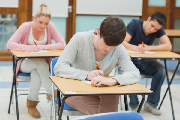 tre studerende sidder i et klasseværelse ved et skrivebord og skriver