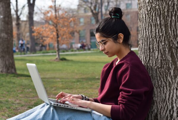 Young,Girl,Student,Sitting,Under,Tree,In,Park,Using,Laptop
